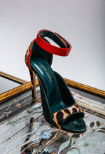 Load image into Gallery viewer, High-heeled sandal with red ankle strap and leopard print sole on a reflective surface.
