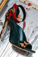 Load image into Gallery viewer, Green high-heeled shoe with red interior and leopard print sole in front of a floral painting.
