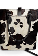 Load image into Gallery viewer, Cow print handbag with black handles on a white background
