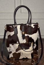 Load image into Gallery viewer, Cow print handbag with brown handles and strap on a marble surface.
