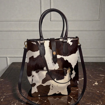 Cow print handbag with brown handles and strap on a marble surface.