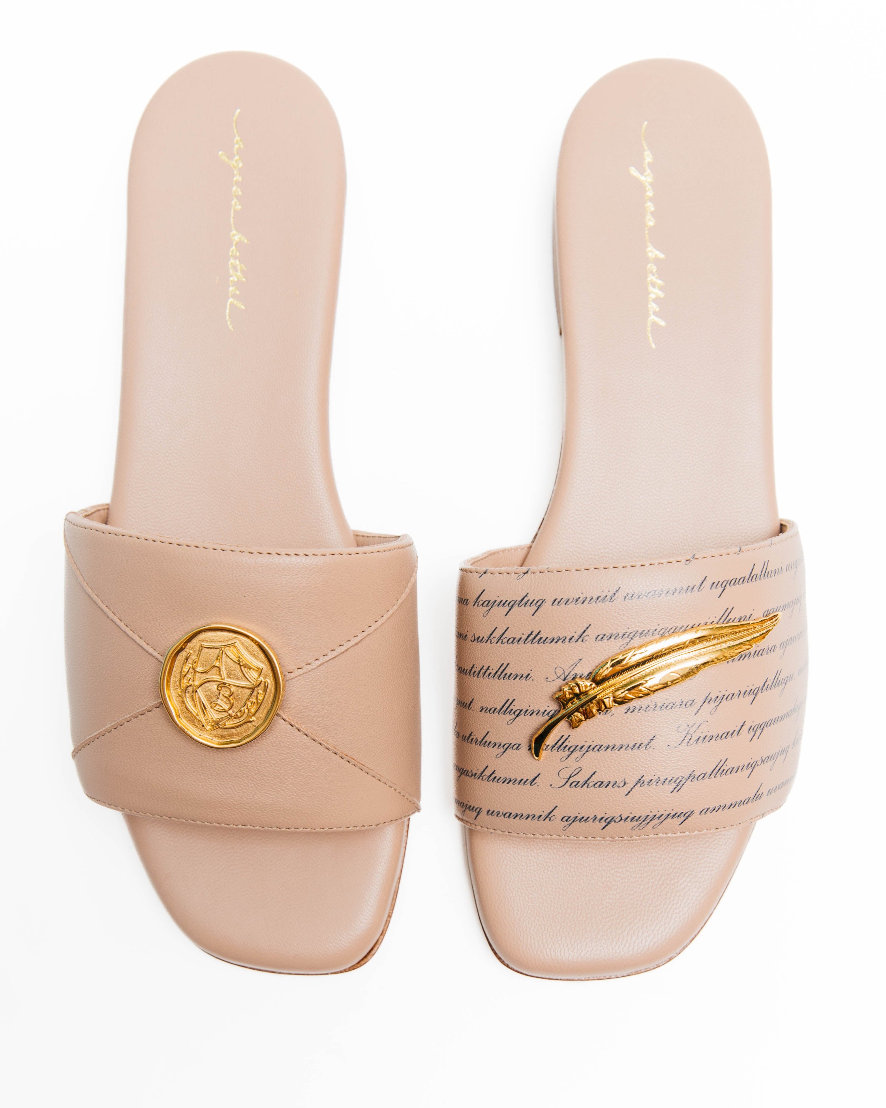 Pair of beige slides with gold accents on a white background