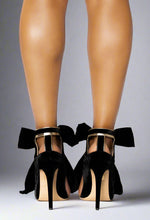 Load image into Gallery viewer, Black high-heeled shoes with bows worn by a person on a white background
