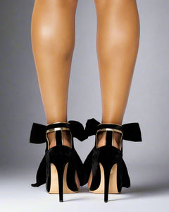 Black high-heeled shoes with bows worn by a person on a white background